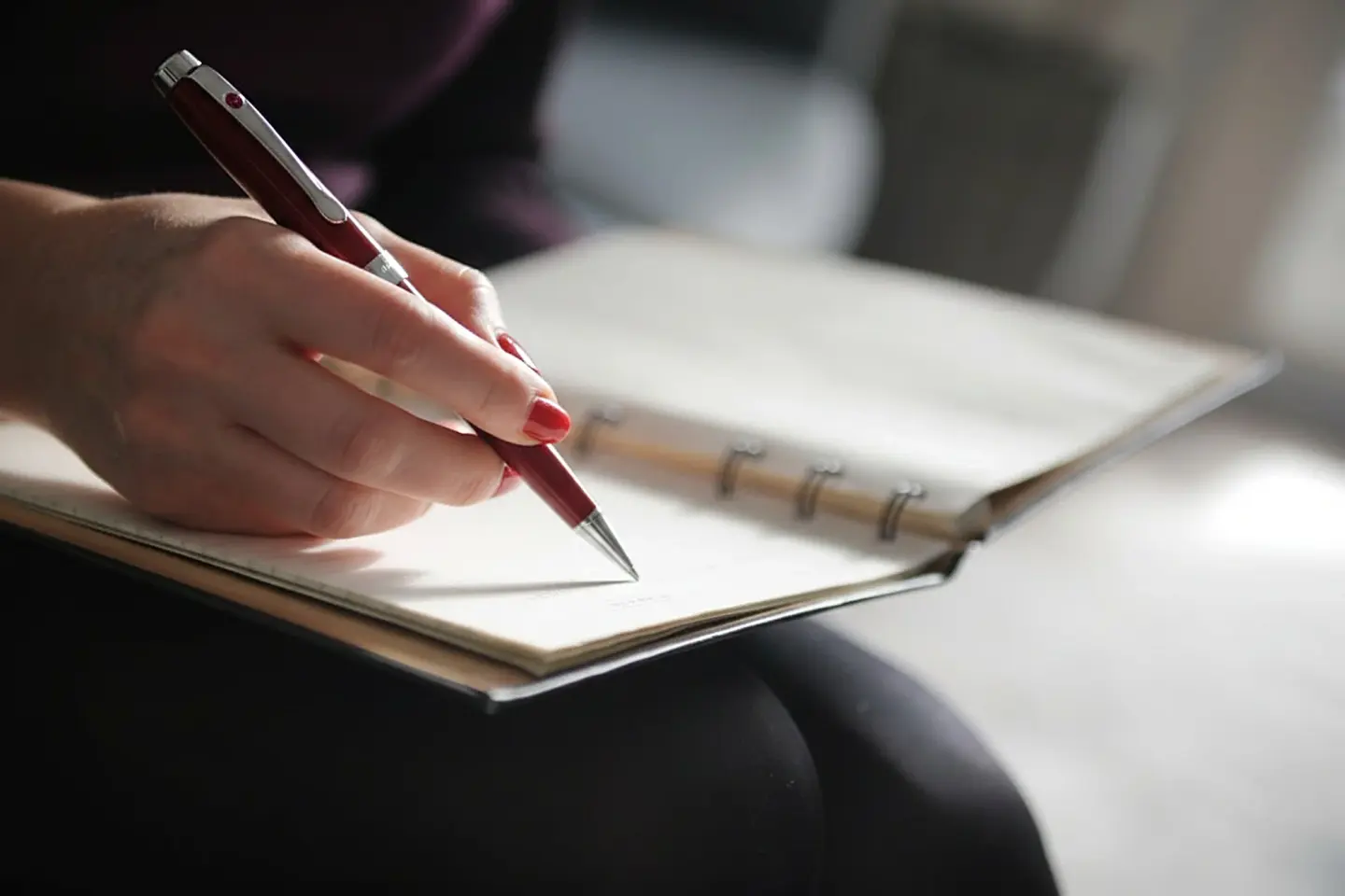 A hand taking notes in a notebook with an elegant pen in a calm, warm office