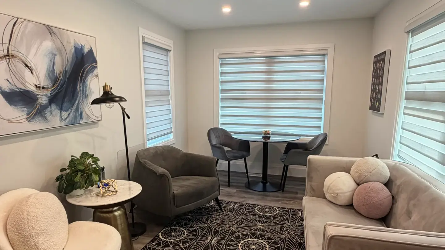 The bright Georgetown therapy studio: a blush sofa and bouclé chairs around a small table by the blind-filtered windows, with blue-and-gold art and a patterned rug